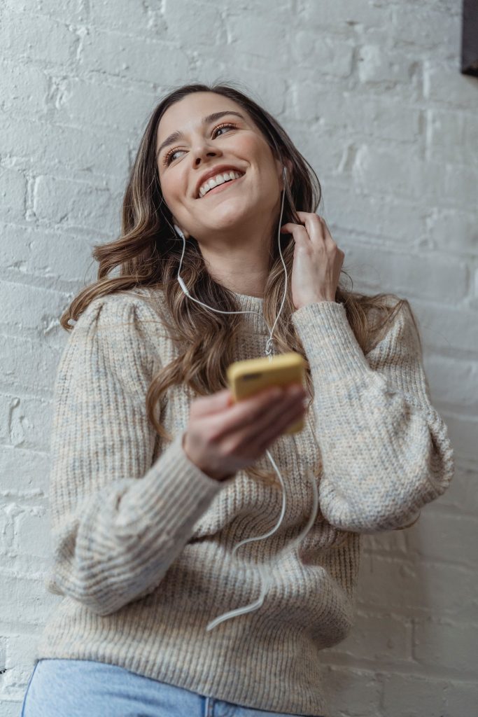 Woman wearing wired earphones beside a brick wall.